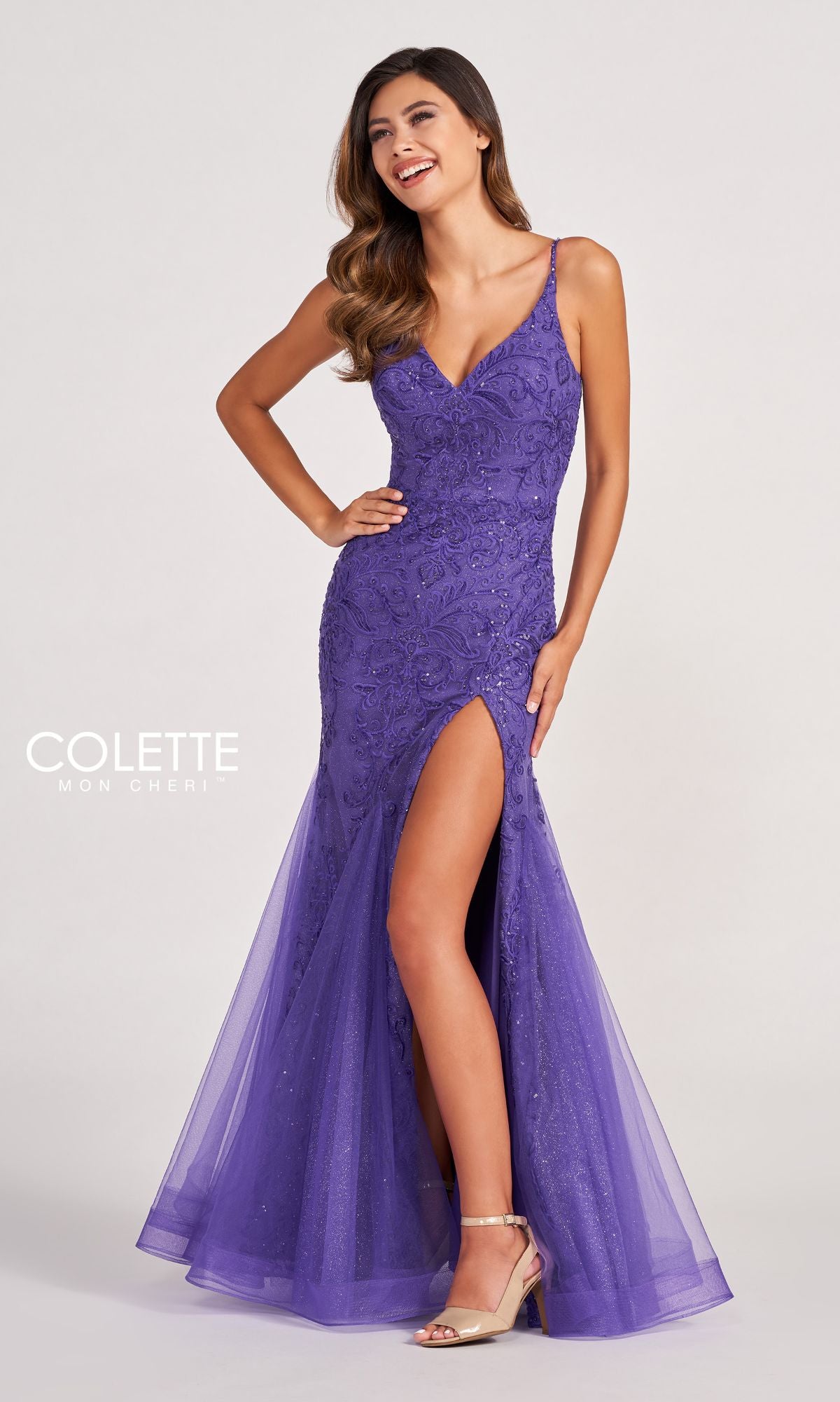 A woman poses confidently with one hand on her hip, wearing the Colette CL2024 Sequin-Lace Cut-Out Long Prom Dress, a fitted purple gown with a thigh-high slit and delicate spaghetti straps.
